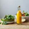 Glass bottle of sunflower dressing oil next to a simple fresh salad on a wooden table